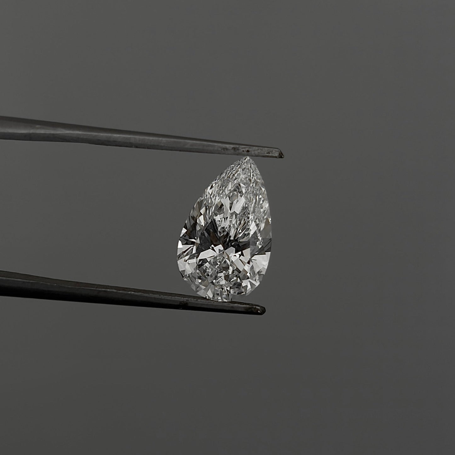 Teardrop-shaped diamond held between tweezers against a gray background