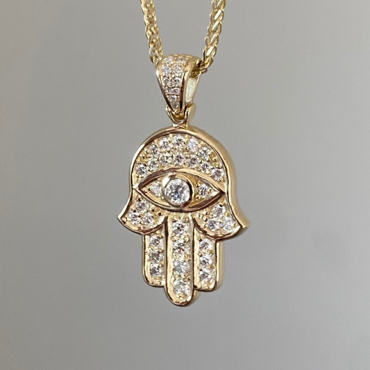 A 14K gold pendant in the shape of a Hamsa Hand with a central eye, studded with lab grown diamonds.