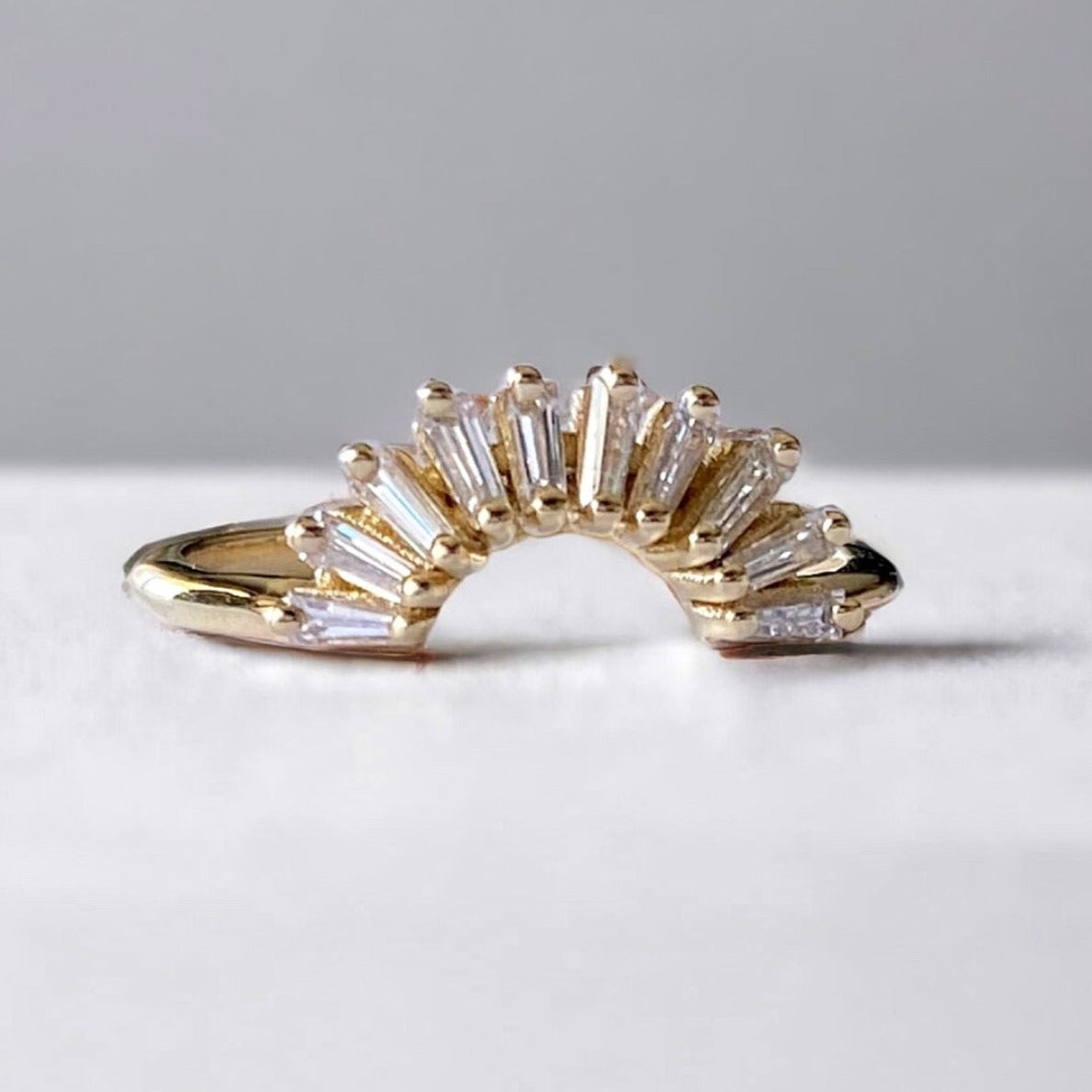 A tapered diamond gold nest ring with multiple bands of diamond accents arranged in a fan-like pattern, set against a neutral background.