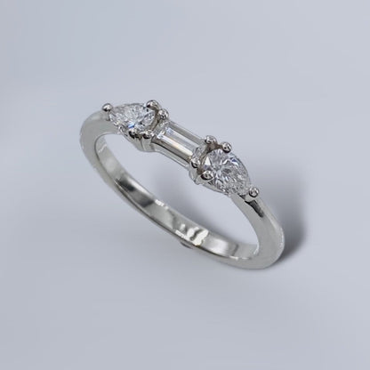 A white gold Art Deco style diamond ring with a central drop-shaped diamond flanked by two baguette-cut diamonds on a plain background.