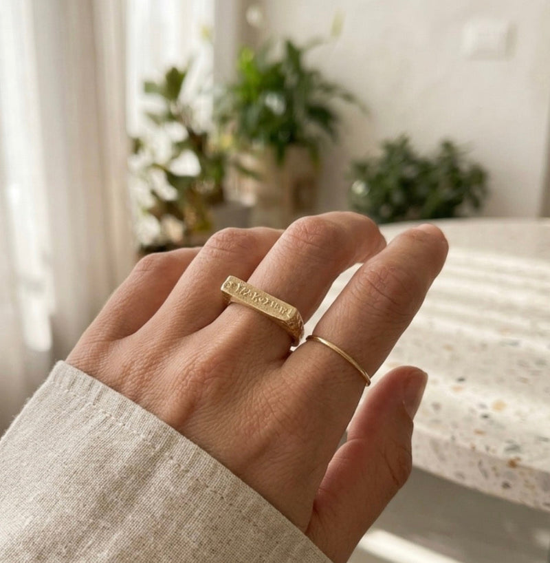 Hand wearing a gold ring with a blurred indoor background