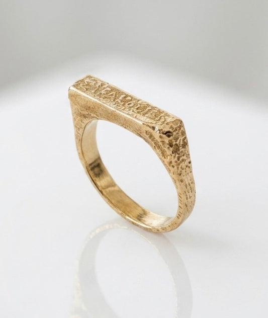 A handcrafted 14K solid gold square ring with a raw texture finish, displayed on a reflective surface.