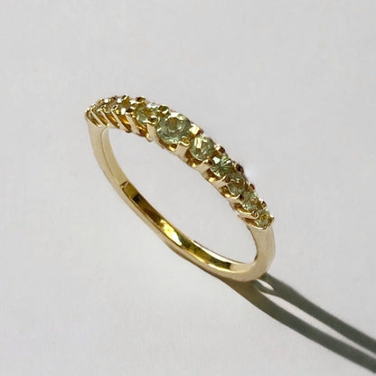 A gold band ring with green sapphire gemstones set around its top edge.