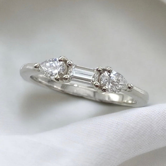 A white gold Art Deco style diamond ring with a central drop-shaped diamond flanked by two baguette-cut diamonds on a plain background.