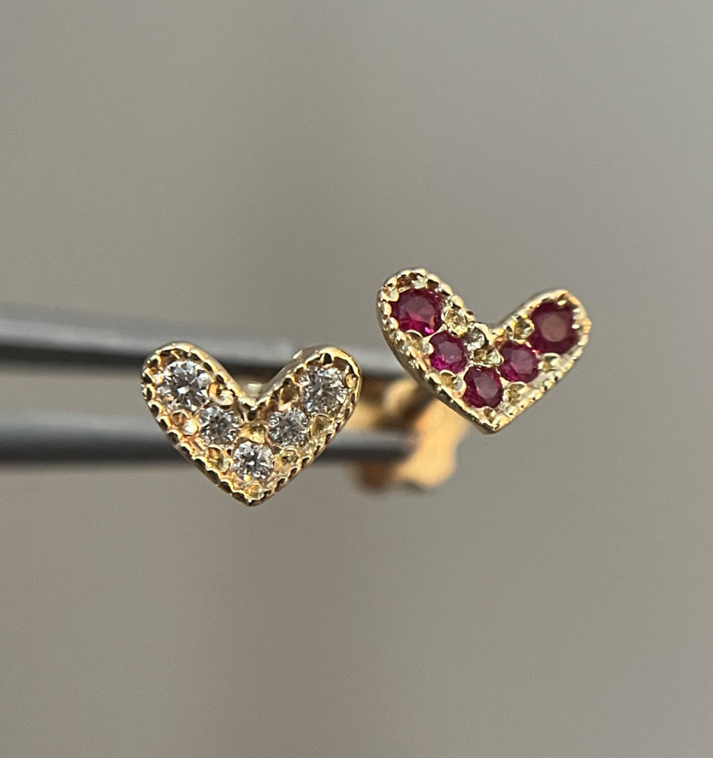 A pair of gold heart-shaped stud earrings, one with diamond accents and the other with ruby stones.