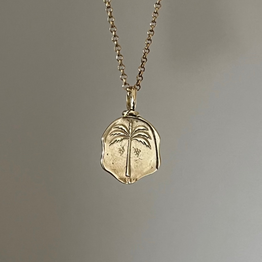 A gold necklace with a coin pendant featuring a palm tree design