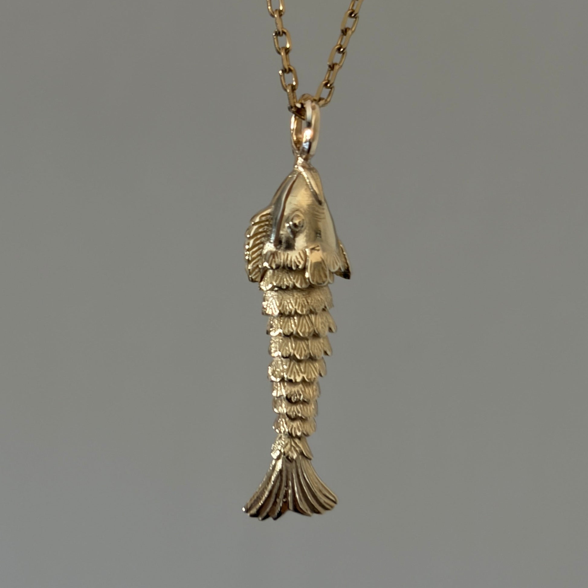 A gold pendant necklace featuring a small, detailed fish charm necklace