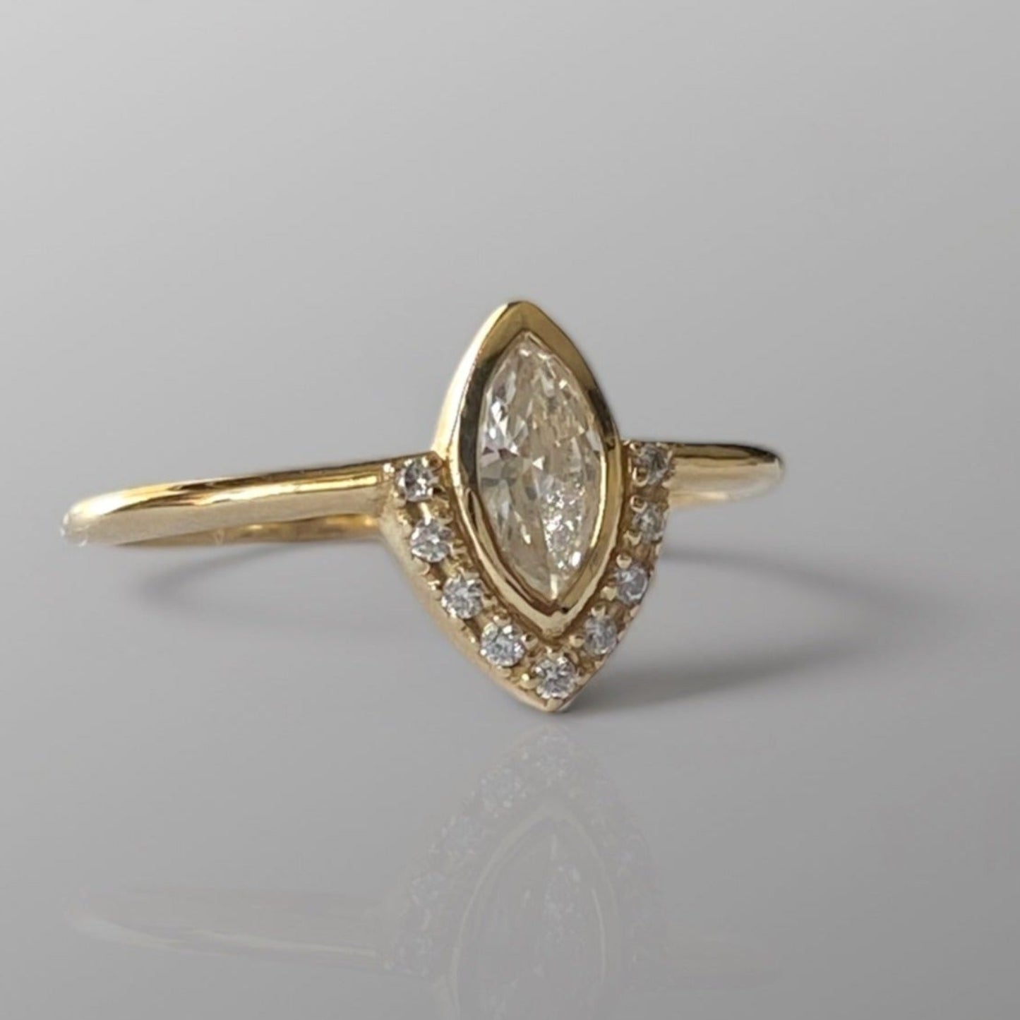 A marquise diamond ring with a central diamond surrounded by smaller diamonds set in a gold band, displayed against a grey background.