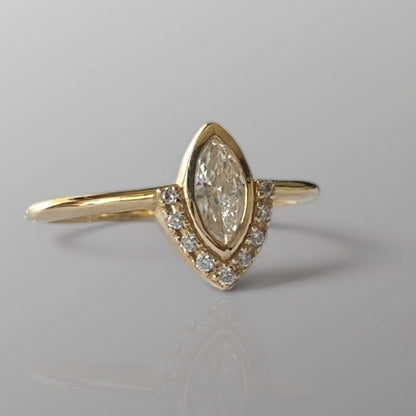 A marquise diamond ring with a central diamond surrounded by smaller diamonds set in a gold band, displayed against a grey background.