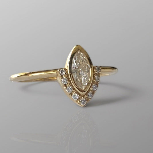 A marquise diamond ring with a central diamond surrounded by smaller diamonds set in a gold band, displayed against a grey background.