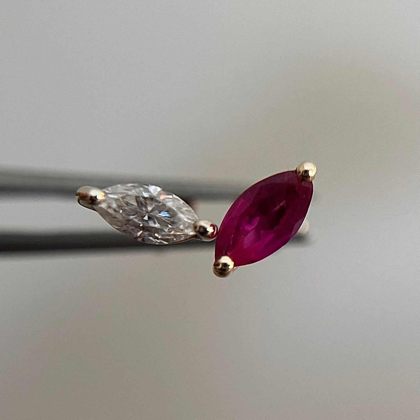 A single marquise-shaped stud earring, featuring a red gemstone, possibly a ruby, set in a smaller frame of white gold with a small natural diamond or ruby stone next to it.