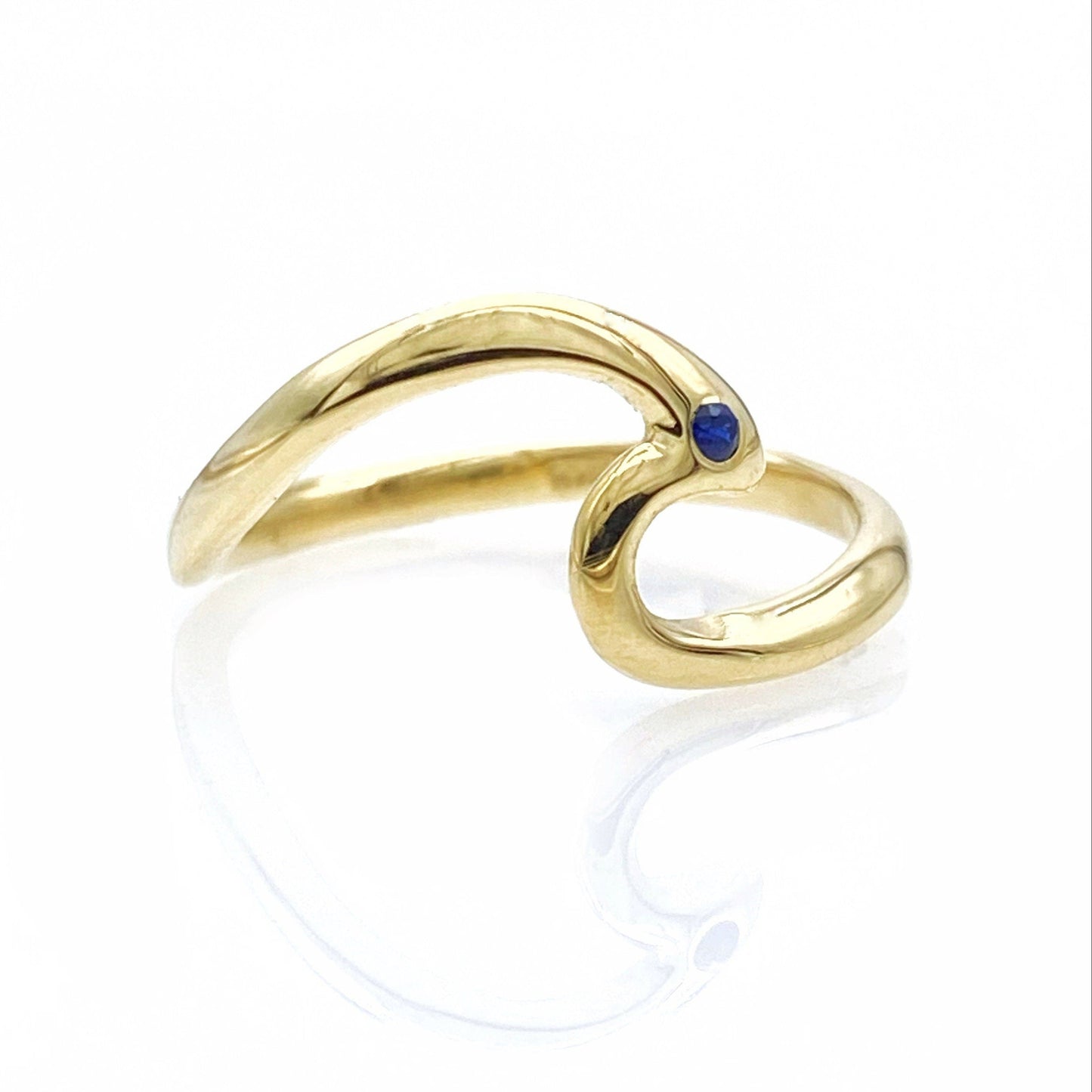 A 14k solid gold wave ring set with one blue sapphire stone, displayed against a white background.