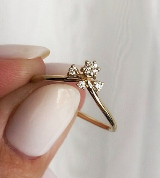 A delicate diamond ring with four natural diamonds set in a gold band, held between fingers.