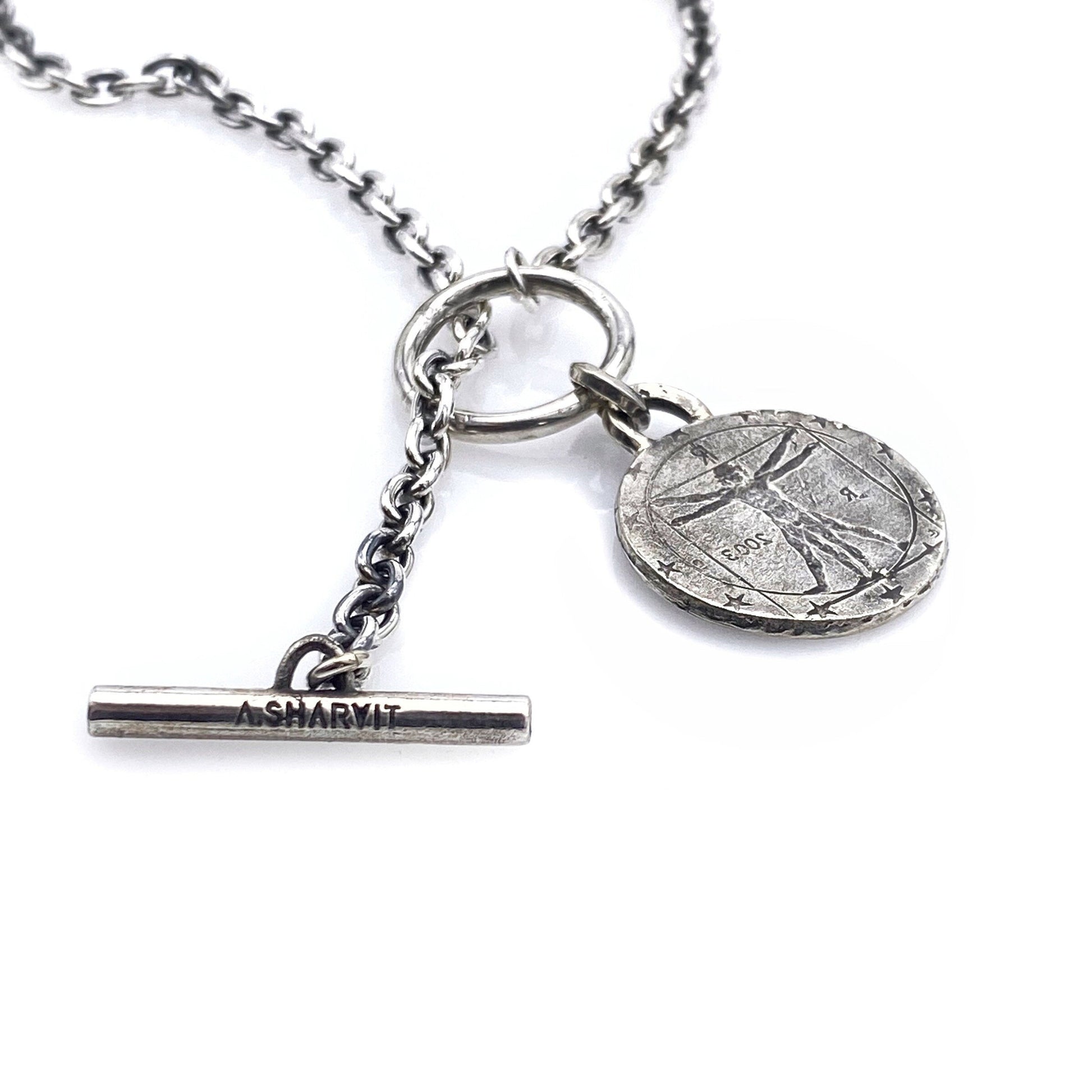 A silver necklace featuring a round coin pendant with an engraving, attached to a silver chain.