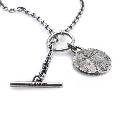 A silver necklace featuring a round coin pendant with an engraving, attached to a silver chain.