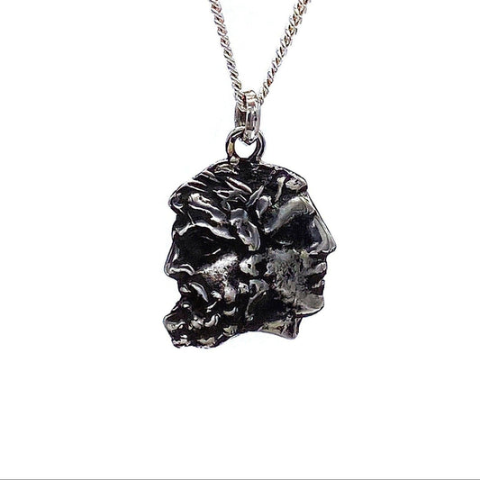 A silver necklace featuring a pendant with two faces, representing the god Janus, in a rustic finish.