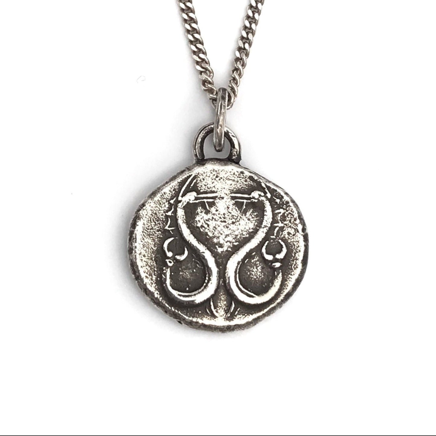 A sterling silver necklace with a polished, rustic finish featuring a round pendant with an engraved serpent design.