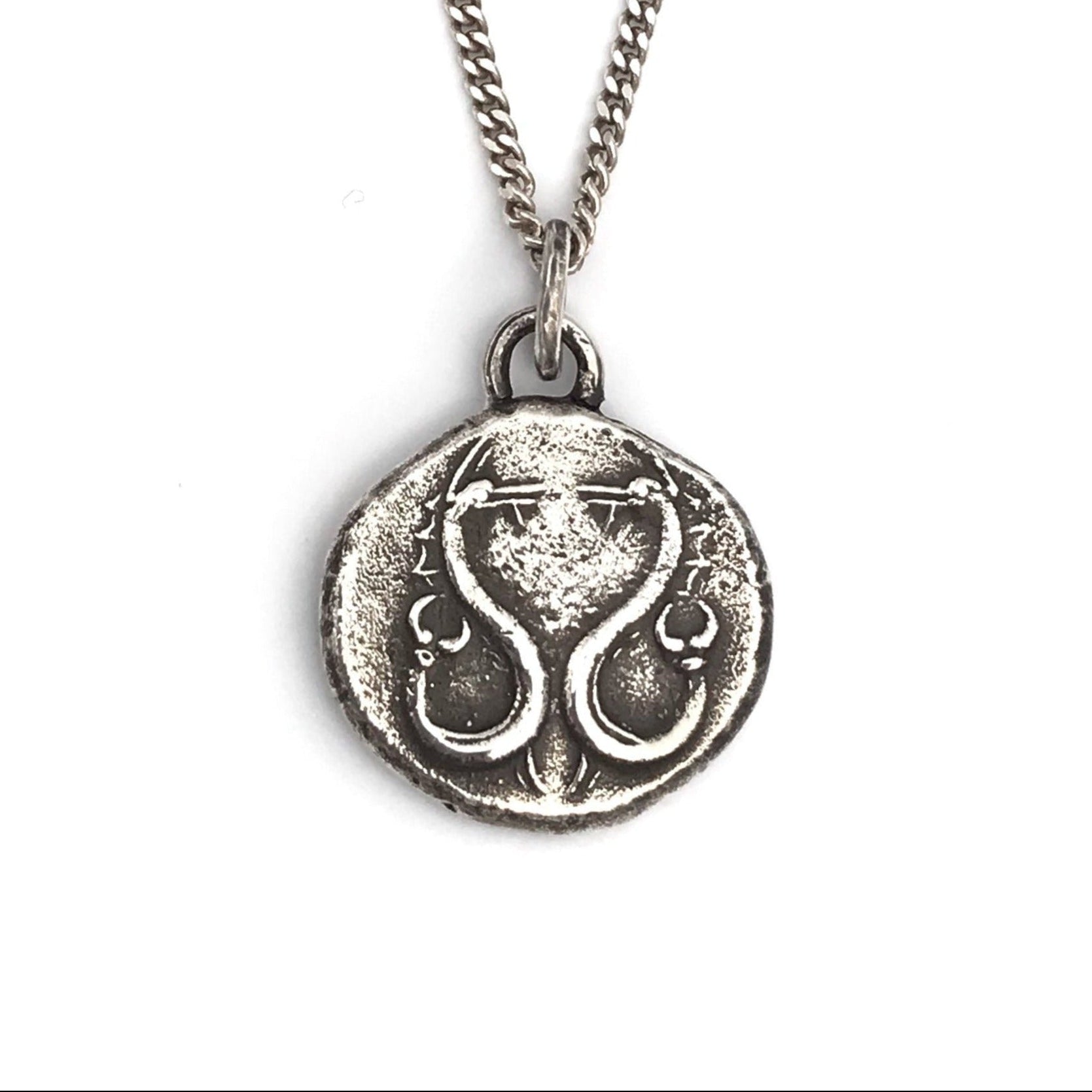 A sterling silver necklace with a polished, rustic finish featuring a round pendant with an engraved serpent design.
