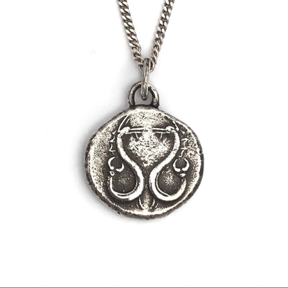 A sterling silver necklace with a polished, rustic finish featuring a round pendant with an engraved serpent design.
